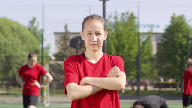 Zuversichtliche-Fußball-Mädchen-posiert-mit-Armen-gekreuzt-auf-Outdoor-Feld