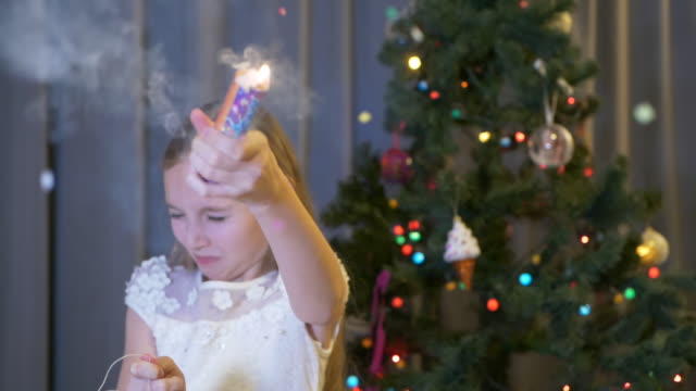 Happy-teenager-girl-blowing-up-holiday-cracker-on-New-Year-tree-background-in-home.-Smiling-girl-teenager-exploding-cracker-on-Christmas-event-on-holiday-tree-background.