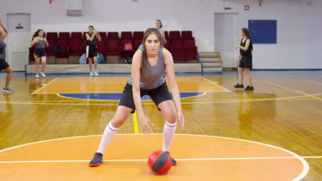 Joven-atleta-femenina-mirando-la-cámara-y-regateando-un-baloncesto