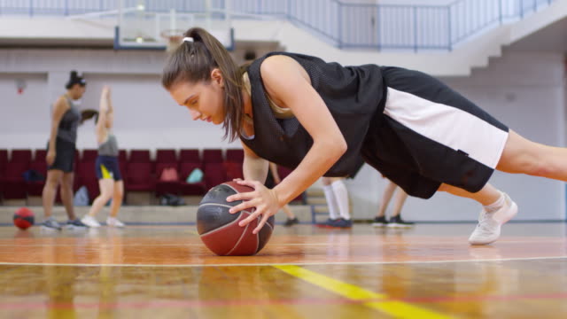 Chica-Joven-haciendo-flexiones-con-baloncesto-mientras-hace-ejercicio-en-la-cancha