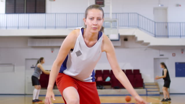 Weibliche-Athletin,-die-auf-die-Kamera-schaut-und-einen-Basketball-zwischen-den-Beinen-dribbelt