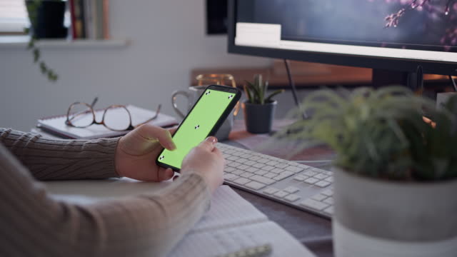 Anonyme-Frau-mit-einem-Smartphone-mit-einem-grünen-Bildschirm-auf-einem-Schreibtisch