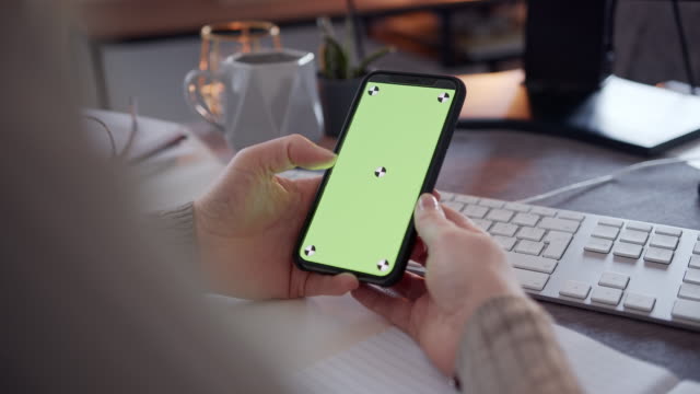 Anonyme-Frau-mit-einem-Smartphone-mit-einem-grünen-Bildschirm-auf-einem-Schreibtisch