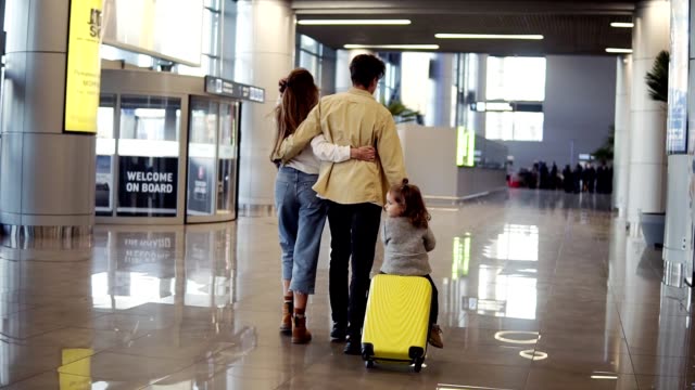 Rückblick-auf-die-moderne-kaukasische-Familie---Mutter,-Vater,-Tochter---zu-Fuß-durch-die-Flughafenhalle-und-Reiten-ihre-Tochter-auf-Koffer-vor-der-Abreise-in-den-Urlaub.-Zeitlupe