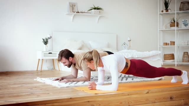 Junges-Paar-macht-Plankenplanke-Übung-zu-Hause-in-gemütlichen-hellen-Schlafzimmer.-Bleiben-Sie-zu-Hause-Konzept