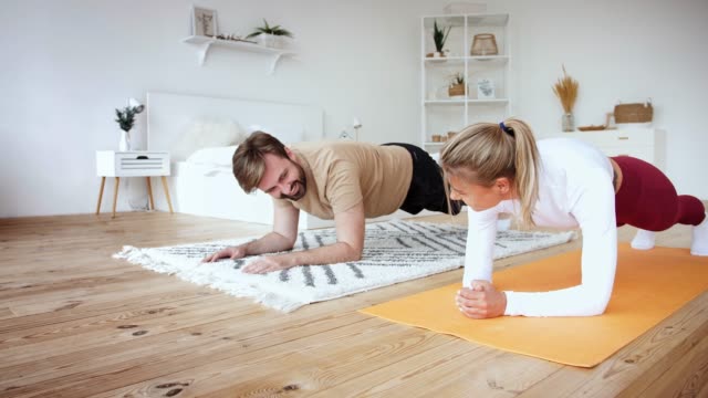Junges-Paar-macht-Plankenplanke-Übung-zu-Hause-in-gemütlichen-hellen-Schlafzimmer,-Zeitlupe.-Bleiben-Sie-zu-Hause-Konzept