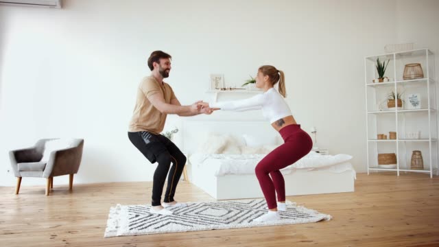 Young-couple-is-doing-squats-excercises-at-home-in-cozy-bright-bedroom,-slow-motion.-Stay-at-home-concept