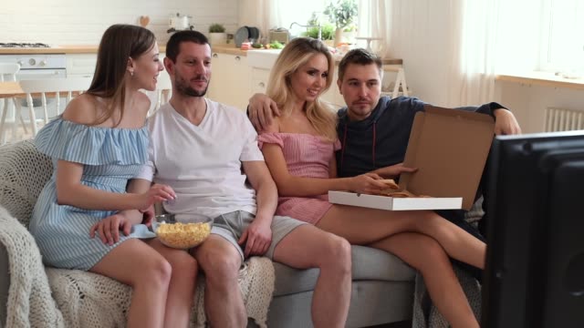 Gruppe-von-Freunden,-die-zusammen-fernsehen-und-Pizza-zu-Hause-auf-dem-Sofa-essen