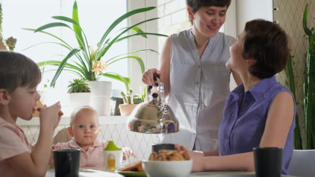 Eine-homosexuelle-lesbische-Familie-mit-zwei-Kindern-und-Müttern-sitzt-in-der-Küche-an-einem-Tisch-und-frühstückt.-Lebensstil.