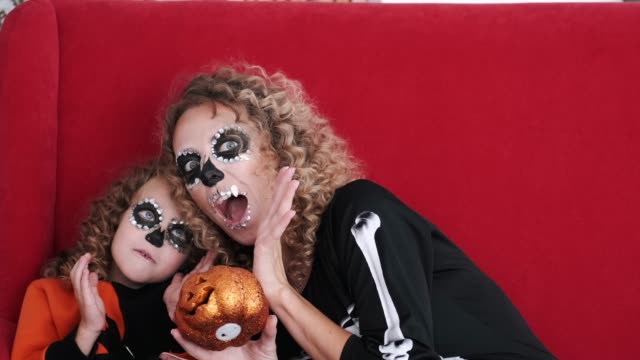 Daughter-and-mom-in-halloween-costumes-play-on-red-sofa