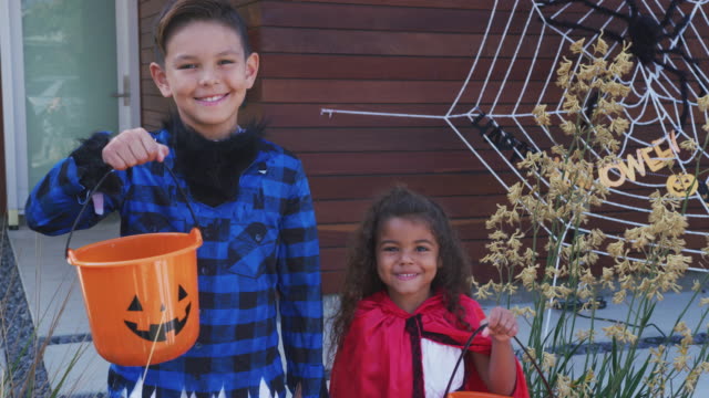 Portrait-Of-Two-Children-Wearing-Fancy-Dress-Outside-House-Collecting-Candy-For-Trick-Or-Treat