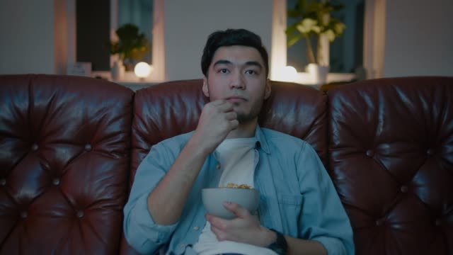 Gelangweilte-asiatische-Männer,-die-auf-dem-Sofa-im-Schlafzimmer-fernsehen.