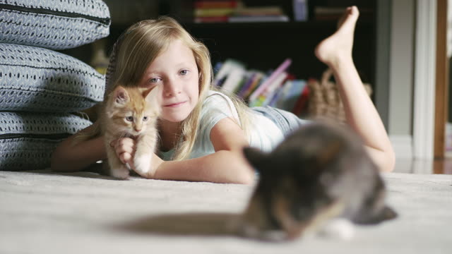 A-little-girl-laying-on-the-floor-holding-a-kitten-and-smiling,-with-another-kitten-in-the-foreground