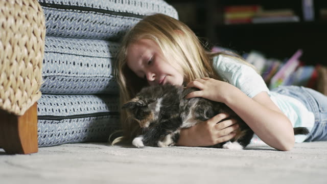 A-little-girl-laying-on-the-floor-and-petting-a-kitten-as-it-tries-to-get-away