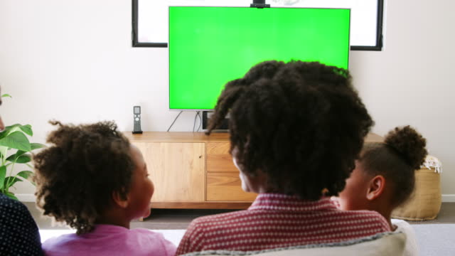 Rear-view-of-young-family-sitting-on-sofa-at-home-and-watching-television