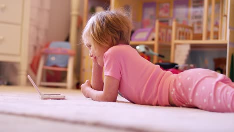 Una-niña-pequeña-que-descansan-en-su-dormitorio-piso-mientras-disfruta-de-un-programa-en-su-portátil-con-sistema-de-juegos