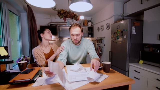 Worried-couple-looking-at-their-bills-in-the-kitchen-at-home.-Man-and-woman-calculating-domestic-accounts