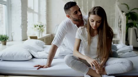 Depressed-young-woman-sitting-in-bed-and-crying-while-her-boylfriend-come-and-embrace-her-and-kiss-in-bedroom-at-home