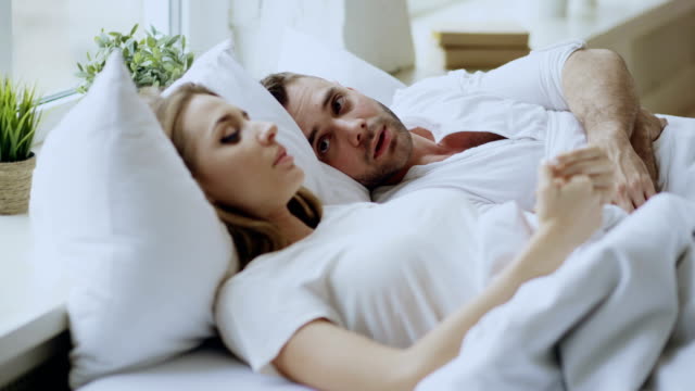 Closeup-of-couple-with-relationship-problems-having-emotional-conversation-while-lying-in-bed-at-home.-Young-woman-turn-away-her-boyfriend