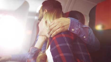 On-a-Commercial-Plane-Handsome-Young-Hispanic-Male-Opens-Window's-Shade-and-Hugs-His-Beautiful-Blonde-Girlfriend-and-they-Romantically-Look-Through-the-Window.-Sun-Shines-through-the-Porthole.