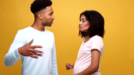 Angry-african-man-having-an-argument-with-his-pregnant-wife-and-she-begins-to-cry-isolated-over-yellow-background