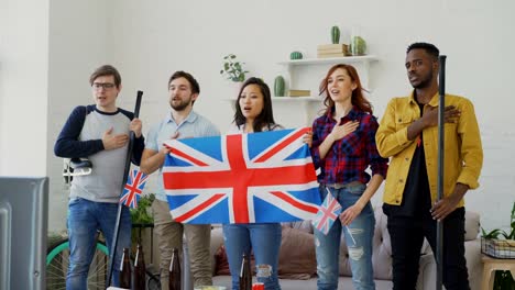 Multi-ethnischen-Gruppe-von-Freunden-hören-und-singen-britische-Nationalhymne-vor-gerade-Sport-Meisterschaft-im-Fernsehen-zusammen-zu-Hause