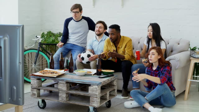 Multi-ethnischen-Gruppe-von-Freunden-Sport-Fans,-die-Fußball-EM-im-Fernsehen-zusammen-Pizza-essen-und-Bier-zu-Hause-beobachten