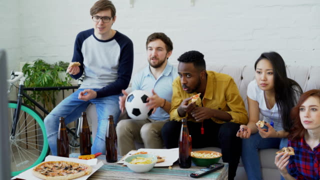 Multi-ethnische-Gruppe-von-Freunden-Sport-Fans,-die-Fußball-EM-im-Fernsehen-zusammen-Pizza-essen-und-Bier-zu-Hause-beobachten