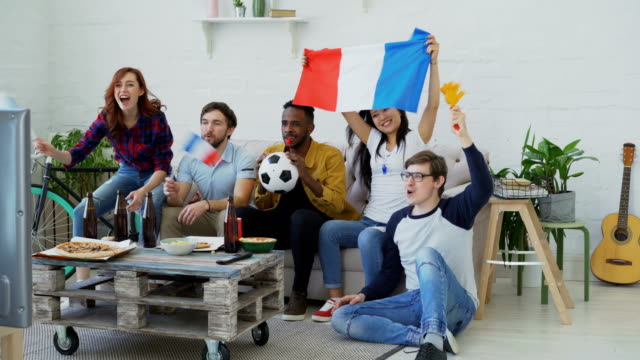Grupo-multiétnico-de-amigos-deportes-aficionados-con-banderas-francesas-ver-Campeonato-de-fútbol-en-la-televisión-juntos-en-casa-y-animar-para-arriba-equipo-favorito