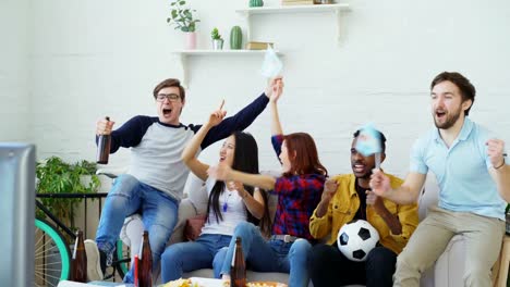 Multi-ethnic-group-of-friends-sports-fans-with-Argentinian-flags-watching-football-championship-on-TV-together-at-home-and-cheering-up-favourite-team