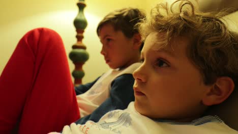 Die-jungen-sitzen-auf-dem-Sofa-vor-dem-Fernseher-hinter-der-Kamera.-4K-candid-Clip-von-Kindern,-die-auf-Bildschirm-zu-Hause