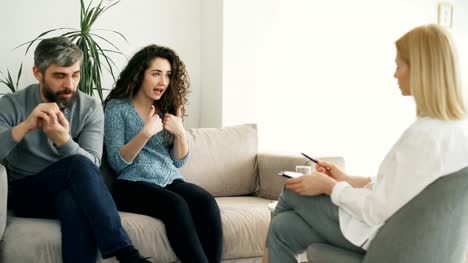 Angry-woman-arguing-and-talking-about-her-husband-to-marriage-counselor.-Young-couple-visiting-professional-psychologist-office