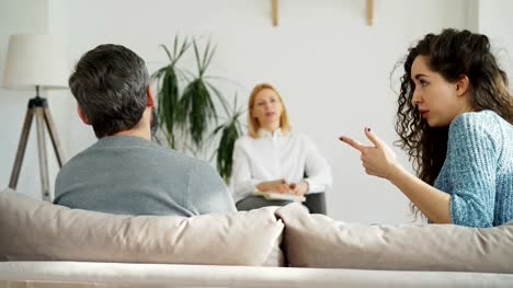 Weibliche-erfahrene-Psychoanalytiker,-zuhören-und-Schreiben-von-Notizen-während-wütend-Ehepaar-Streit-und-Zank-bei-professionellen-Psychologen-und-Ratgeber-Standesamt-besuchen