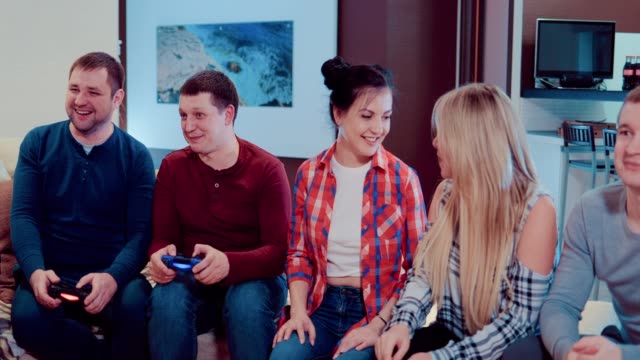 Compañía-de-los-amigos-de-relajarse-en-el-sofá-jugando-videojuegos-y-divirtiéndose-en-piso-moderno