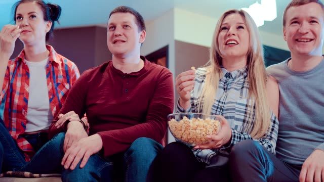 Company-of-friends-watching-a-comedy-on-TV,-laughing-and-eating-popcorn