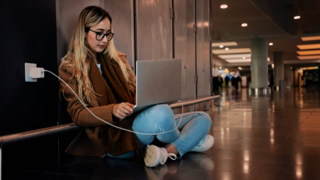 Young-woman-traveler-charging-laptop-and-working-at-airport