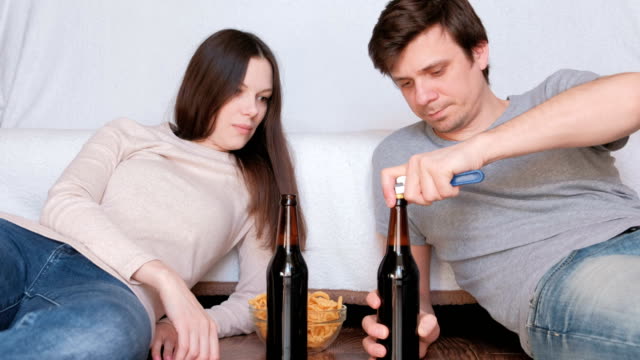 Termin.-Paar-Mann-und-Frau-liegen-auf-dem-Boden-zu-Hause-essen-Chips-und-Bier-zu-trinken.-Mann-öffnet-Bierflasche.