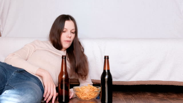 Couple-of-young-man-and-woman-eating-chips-drinking-beer-and-watching-TV.