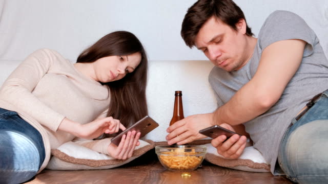 Paar-Mann-und-Frau-in-ihre-Handys,-trinken-Bier-und-Essen-Chips-messaging.