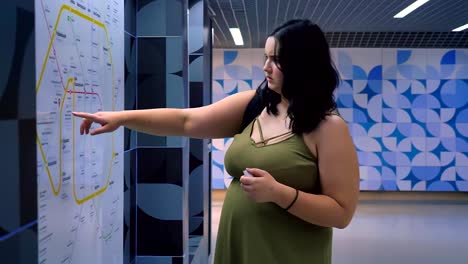 Charming-overweight-female-tourist-looking-at-map,-standing-in-modern-underground-subway,-complicated-expression-on-her-face
