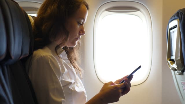 Frau-mit-Smarthone-sitzen-im-Flugzeug-in-der-Nähe-von-Fenster