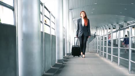 Slow-motion-shot-of-Young-attractive-Asian-business-woman-dragging-a-wheeled-suitcase-at-the-airport-ramp-way-for-business-trip