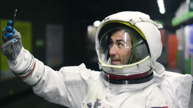 An-astronaut-dressed-man-uses-the-smartphone-to-call-and-send-messages.-The-astronaut-smiles-while-looking-at-the-phone-in-his-hand.