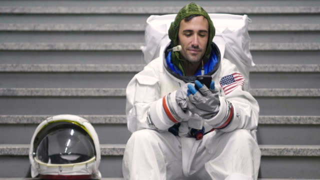 Ein-Astronaut-gekleidet-Mann-nutzt-das-Smartphone-anrufen-und-Nachrichten-senden.-Der-Astronaut-lächelt-beim-Betrachten-des-Telefons-in-der-Hand.