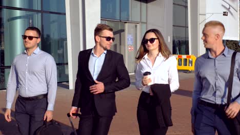 Group-of-young-business-person-walking-to-airport-at-sunny-day.-Colleagues-being-on-his-way-to-business-trip.-Business-people-going-to-terminal-and-talking.-Success-concept.-Slow-motion-Close-up