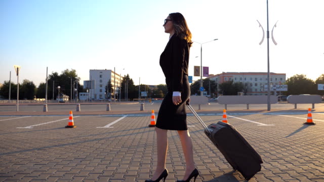 Young-businesswoman-going-to-taxi-parking-from-the-airport-with-her-suitcase.-Lady-walking-with-her-suitcase-along-street.-Travel-concept.-Side-view-Slow-motion-close-up
