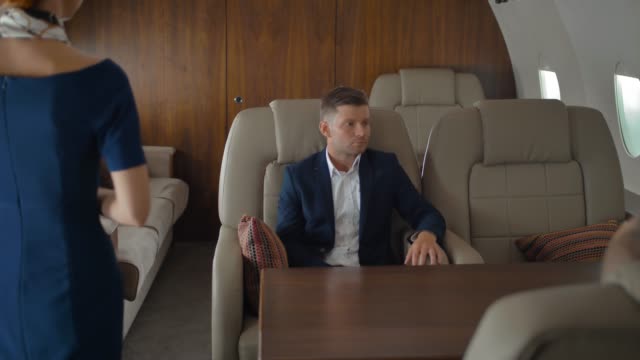 Businesspeople-inside-of-private-jet-relaxing-while-flying-and-speaking-with-stewardess