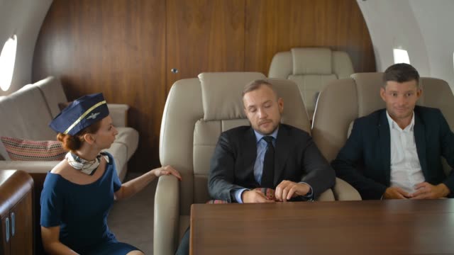Three-businesspeople-inside-of-private-jet-relaxing-and-speaking-with-stewardess