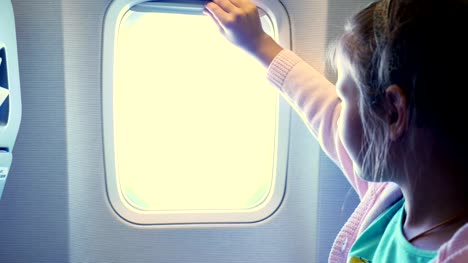 Close-up.-Kind-Mädchen-wirft-das-Bullauge-Vorhang-in-der-Flugzeugkabine,-von-dort-strahlt-ein-helles-Licht.-Mädchen-auf-der-Suche-durch-Flugzeug-Fenster-anzeigen,-Himmel-und-Wolken-und-Landschaft-unter