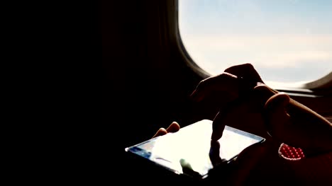 Close-up.-los-rayos-del-sol-se-reflejan-en-el-teléfono.-silueta-oscura-de-las-manos-del-niño-y-el-teléfono-móvil-contra-iluminador-del-avión.-Niño-con,-juego-de-juegos-en-smartphone,-teléfono-tableta-en-cabina-de-avión